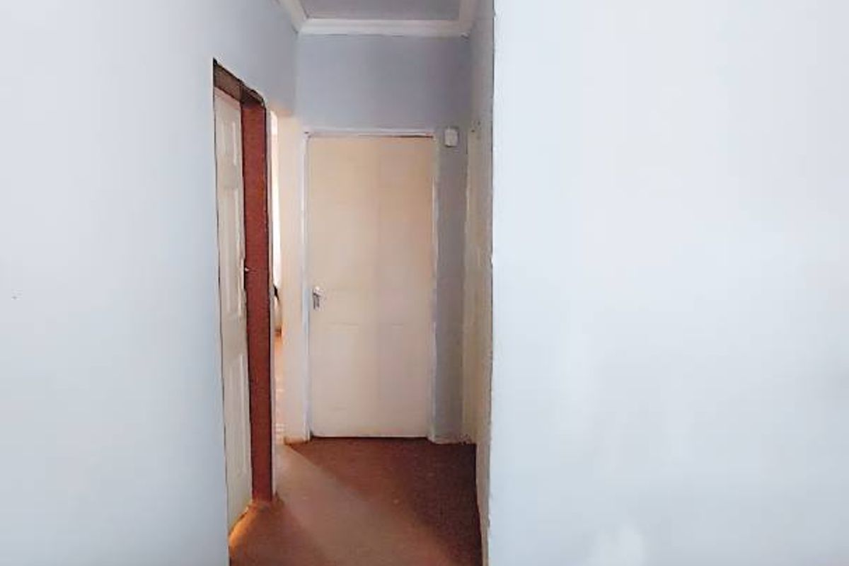 A sparse kitchen area featuring a standalone stove and access to a hallway, requiring cosmetic updates to flooring and wall finishes.