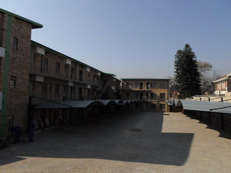 Exterior view of a multi-story apartment complex featuring face brick construction, covered parking bays, and a paved central courtyard area.