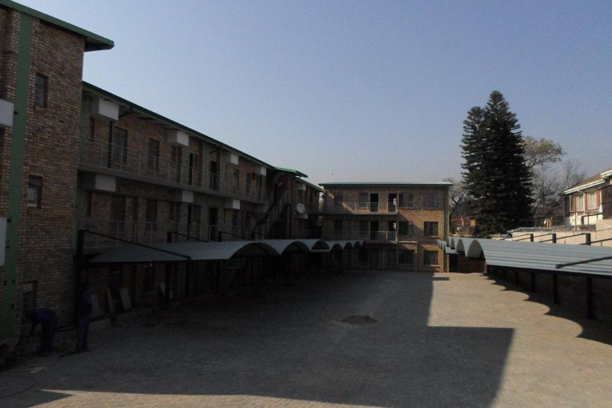 Exterior view of a multi-story apartment complex featuring face brick construction, covered parking bays, and a paved central courtyard area.