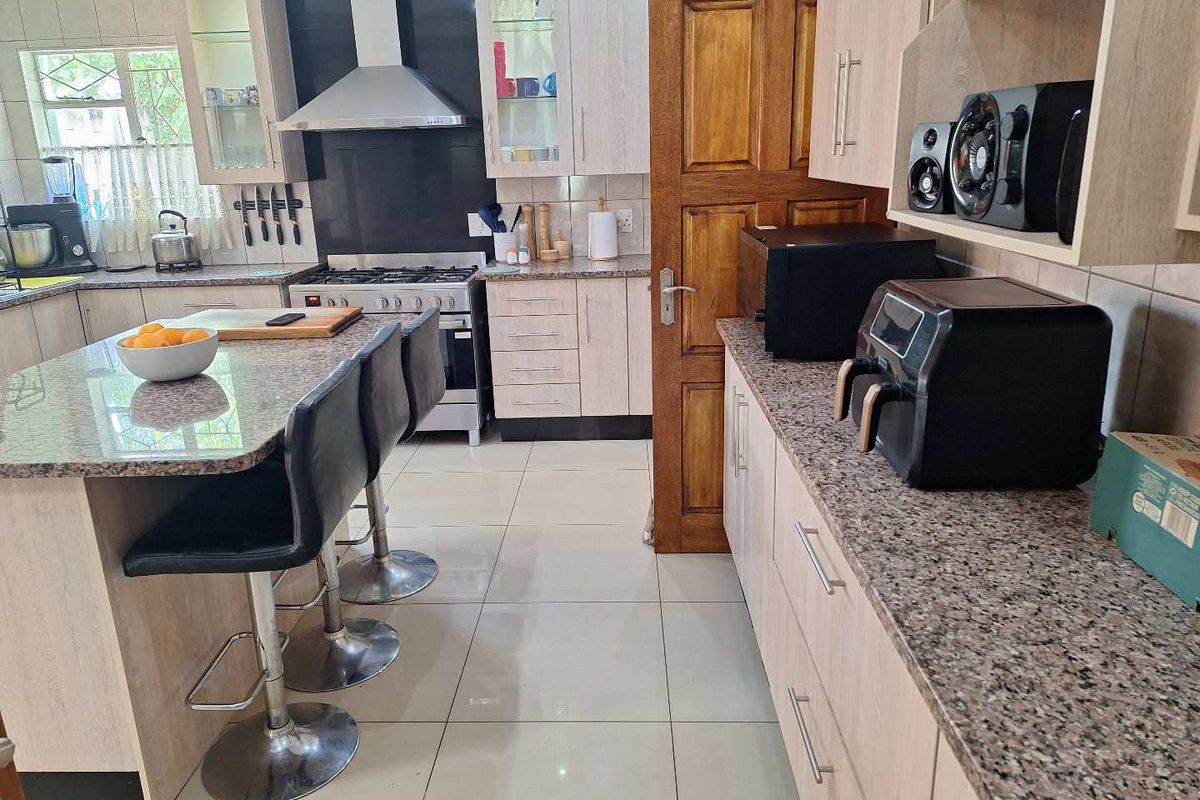 A functional kitchen featuring granite countertops, light wood cabinetry, a central island, and a gas stove with an extractor fan.