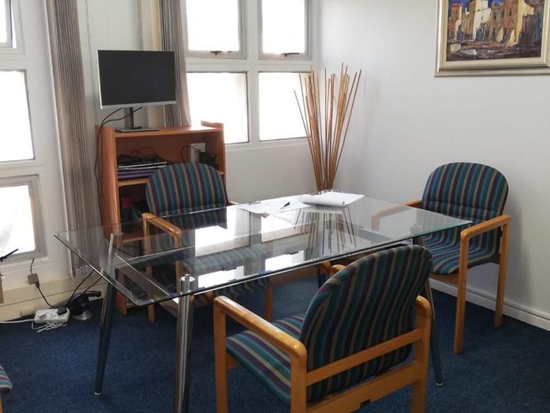 A functional office space featuring blue carpeting, vertical window blinds, and a wall-mounted air conditioning unit.