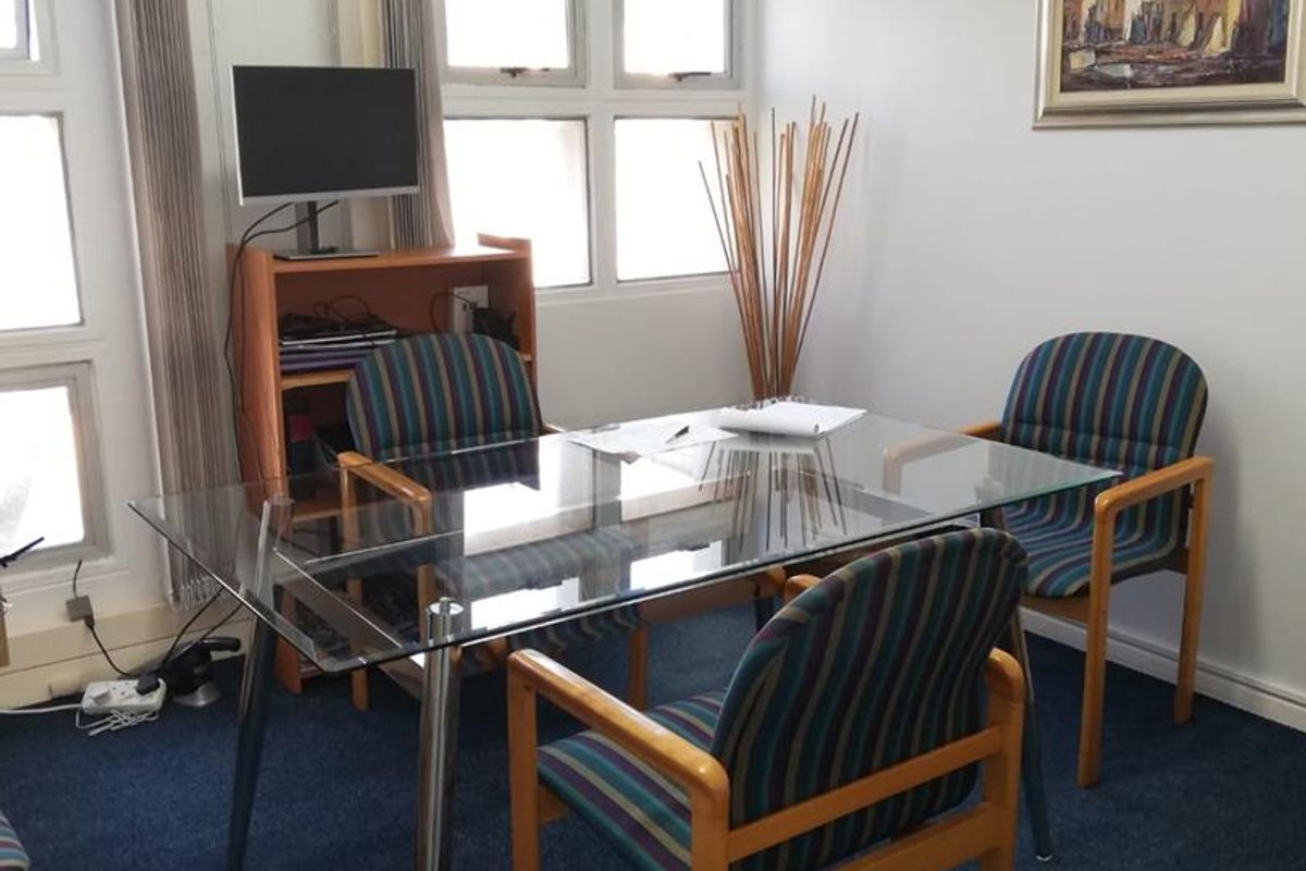 A functional office space featuring blue carpeting, vertical window blinds, and a wall-mounted air conditioning unit.