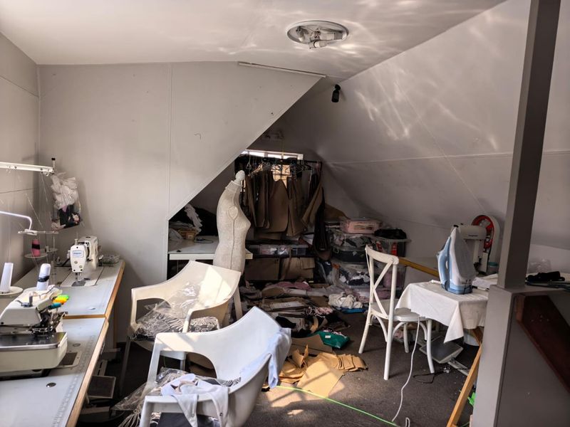 An attic-style office space featuring sloped ceilings, built-in work surfaces, and a recessed storage area, currently utilized as a sewing workshop.