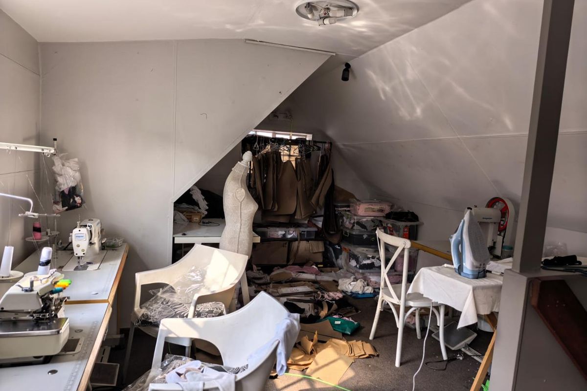 An attic-style office space featuring sloped ceilings, built-in work surfaces, and a recessed storage area, currently utilized as a sewing workshop.