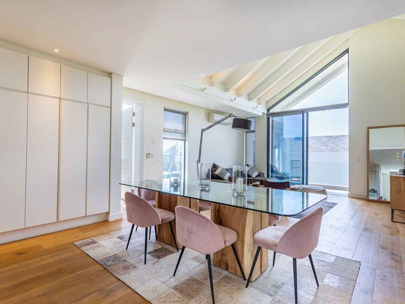 Bright open-plan living and dining area featuring hardwood floors, exposed timber ceiling beams, extensive built-in cabinetry, and large sliding doors leading to a balcony.