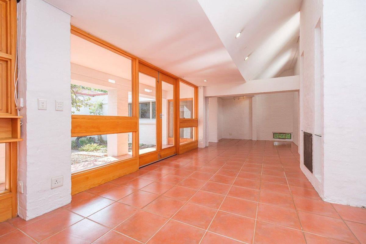 Spacious living area featuring terracotta floor tiles, vaulted ceilings with recessed lighting, and large timber-framed glass doors opening to the garden.