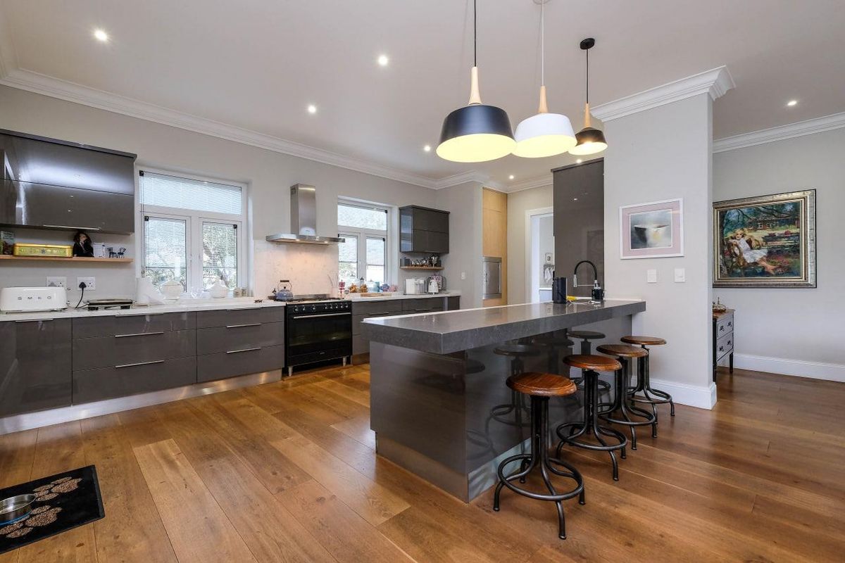 Modern kitchen featuring high-gloss cabinetry, stone countertops, a central island with breakfast bar seating, and premium built-in appliances on hardwood flooring.