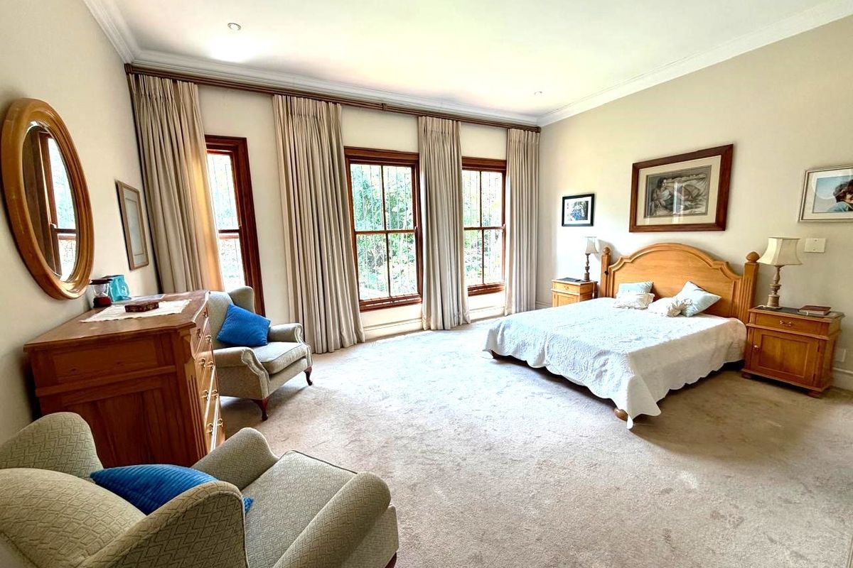 Spacious bedroom featuring neutral carpeting, decorative cove cornicing, and large timber-framed windows with security bars, offering a bright and comfortable living space.