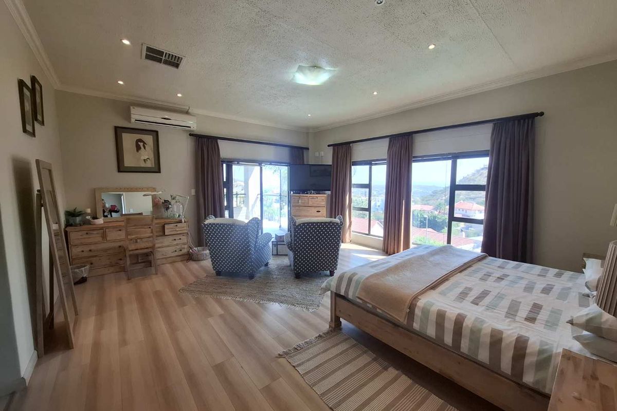 Spacious bedroom featuring light laminate flooring, recessed lighting, split-system air conditioning, and large windows with access to a balcony and scenic views.