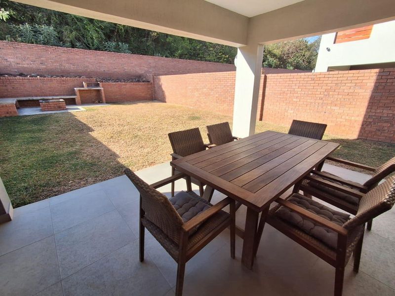 A covered patio area featuring tiled flooring and a built-in brick braai, overlooking a private garden with brick boundary walls.
