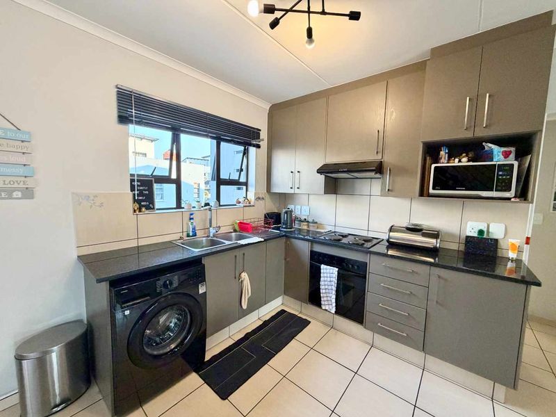 A functional kitchen featuring modern grey cabinetry, granite countertops, a built-in oven with hob, and tiled flooring with a double basin sink.