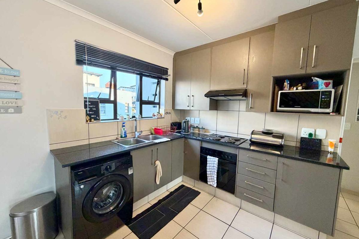 A functional kitchen featuring modern grey cabinetry, granite countertops, a built-in oven with hob, and tiled flooring with a double basin sink.