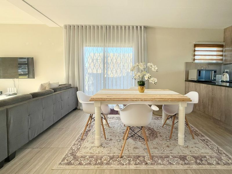 An open-plan living and dining area featuring tiled floors, modern kitchen cabinetry with stone countertops, and a sliding door leading to the exterior.