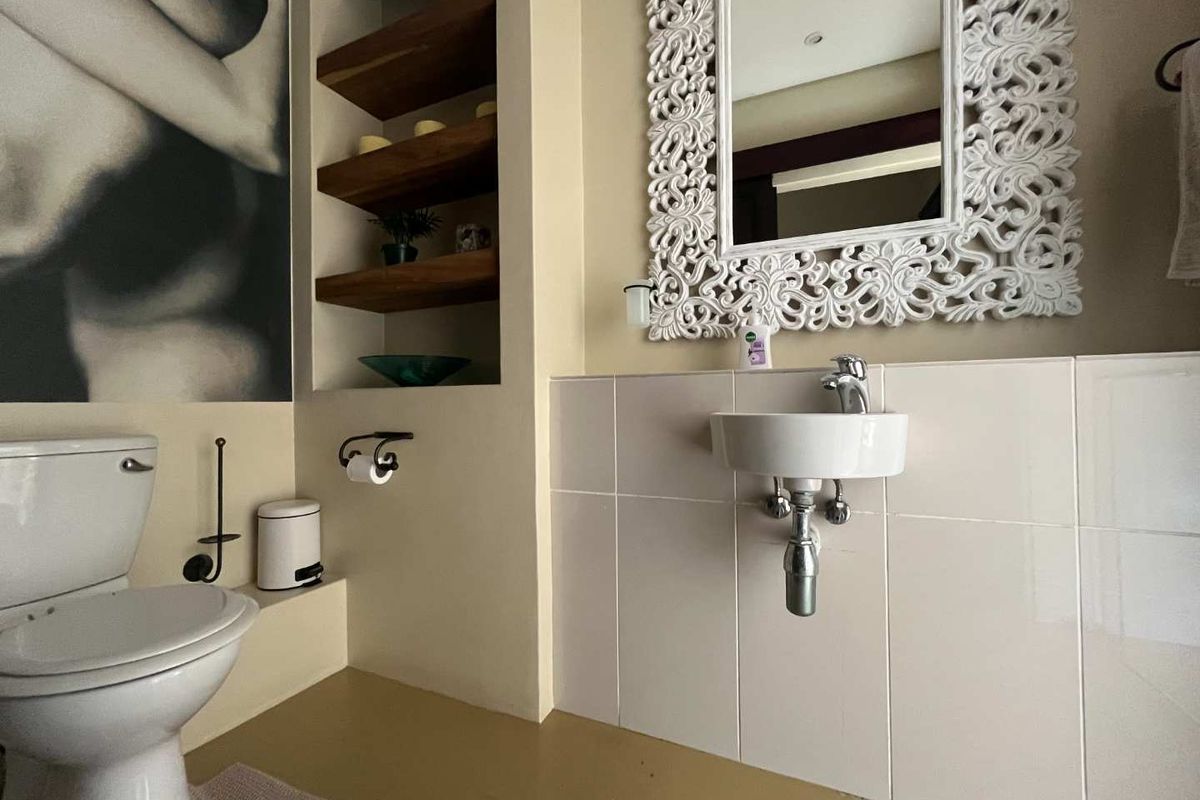 A compact bathroom featuring a wall-mounted basin, a standard toilet, and built-in recessed timber shelving.