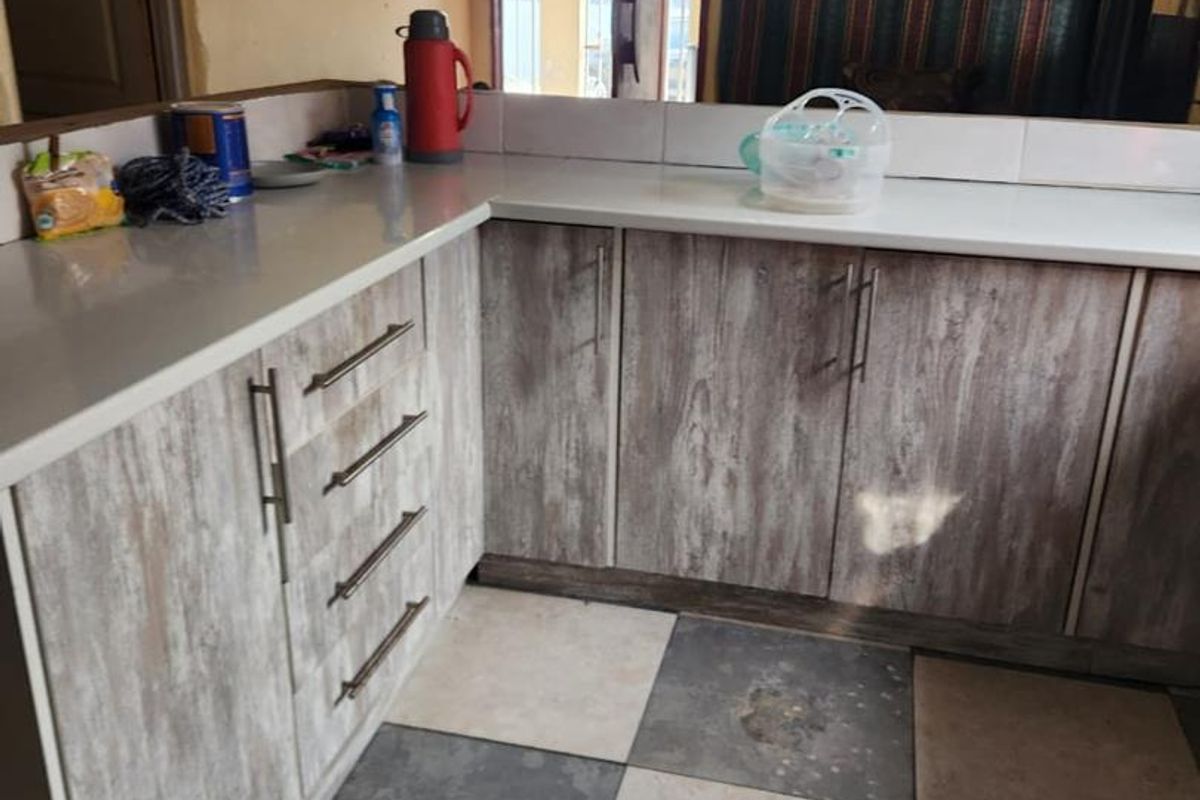 A kitchen area featuring laminate cabinetry, stone countertops, and a checkered tiled floor, currently showing signs of wear and unfinished ceiling surfaces.