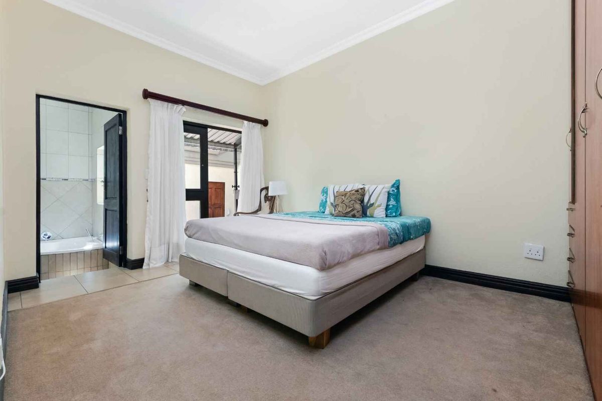 Spacious bedroom featuring neutral carpeting, built-in cupboards, and direct access to an en-suite bathroom and outdoor area.
