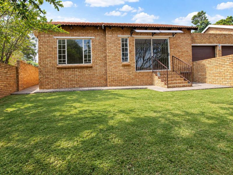 Rear view of the townhouse featuring a face brick facade, a well-maintained lawn, paved walkway, and a sliding door with security gate access.
