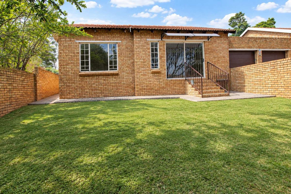 Rear view of the townhouse featuring a face brick facade, a well-maintained lawn, paved walkway, and a sliding door with security gate access.