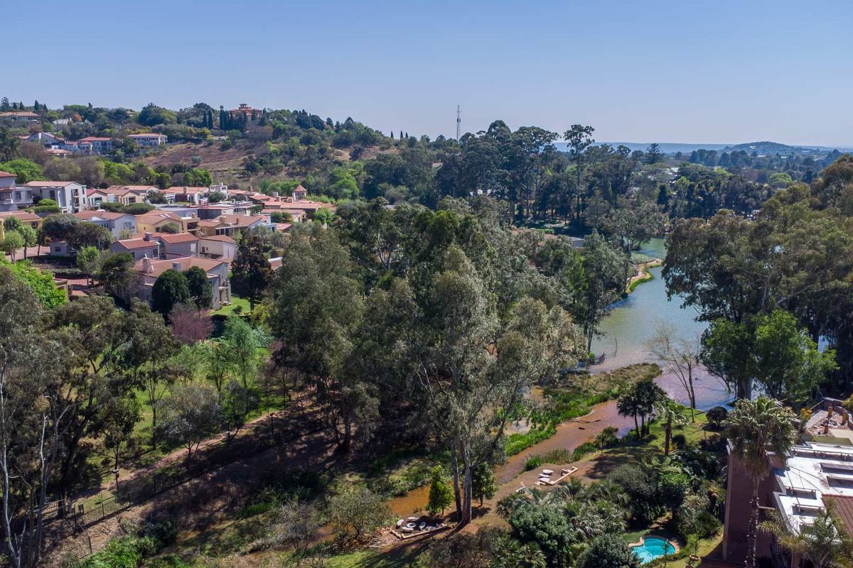 Aerial view of the property showcasing the surrounding lush landscape, mature trees, nearby river, and residential estate setting.