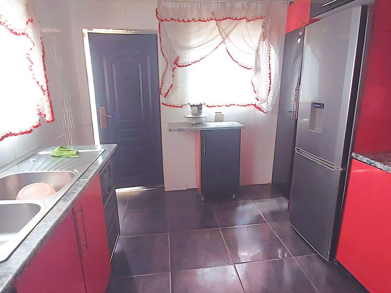 A functional kitchen featuring red cabinetry, laminate countertops, a double bowl stainless steel sink, and built-in oven with tiled flooring.