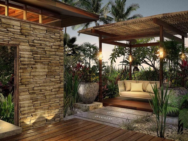 A beautifully landscaped outdoor patio featuring natural stone cladding, timber decking, and a covered pergola, creating a serene and luxurious tropical retreat.