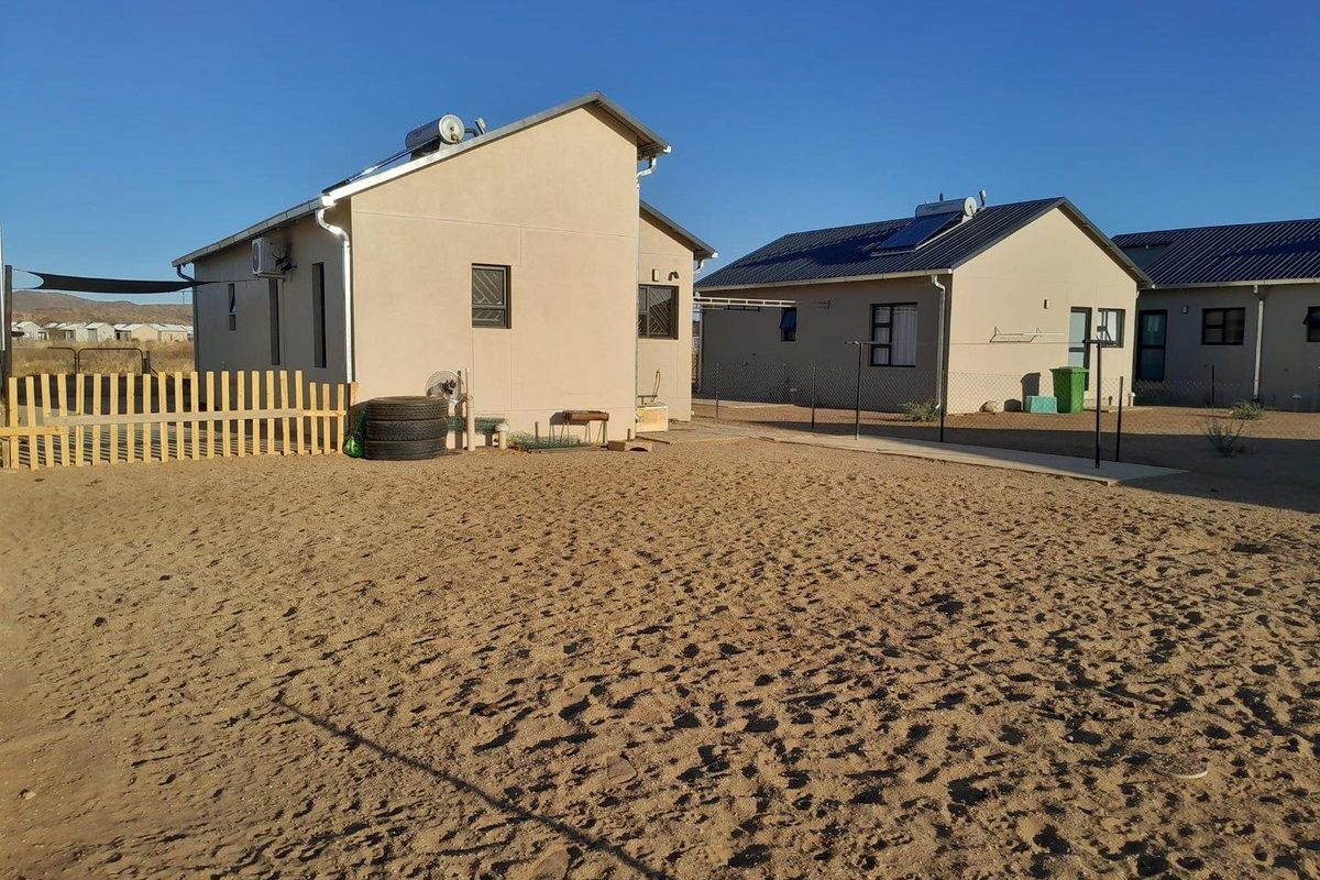 Rear view of the property featuring a detached house with a solar geyser, paved walkway, and a large, open sandy yard area.