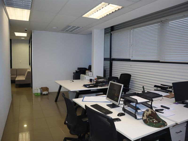 A functional office space featuring tiled flooring, suspended ceilings with recessed lighting, and large windows equipped with venetian blinds.