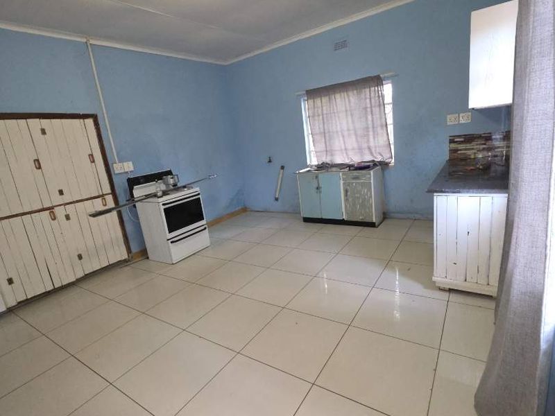 A functional kitchen space featuring tiled flooring, basic cabinetry, and a freestanding stove, offering potential for modernization and cosmetic updates.