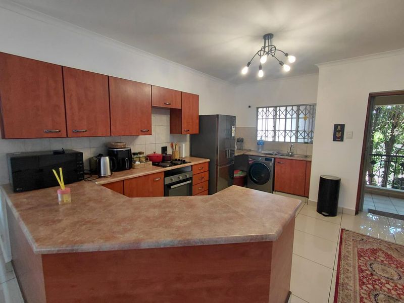 A functional kitchen featuring wood-look laminate cabinetry, ample countertop space, built-in oven, and tiled flooring with direct access to an outdoor balcony area.