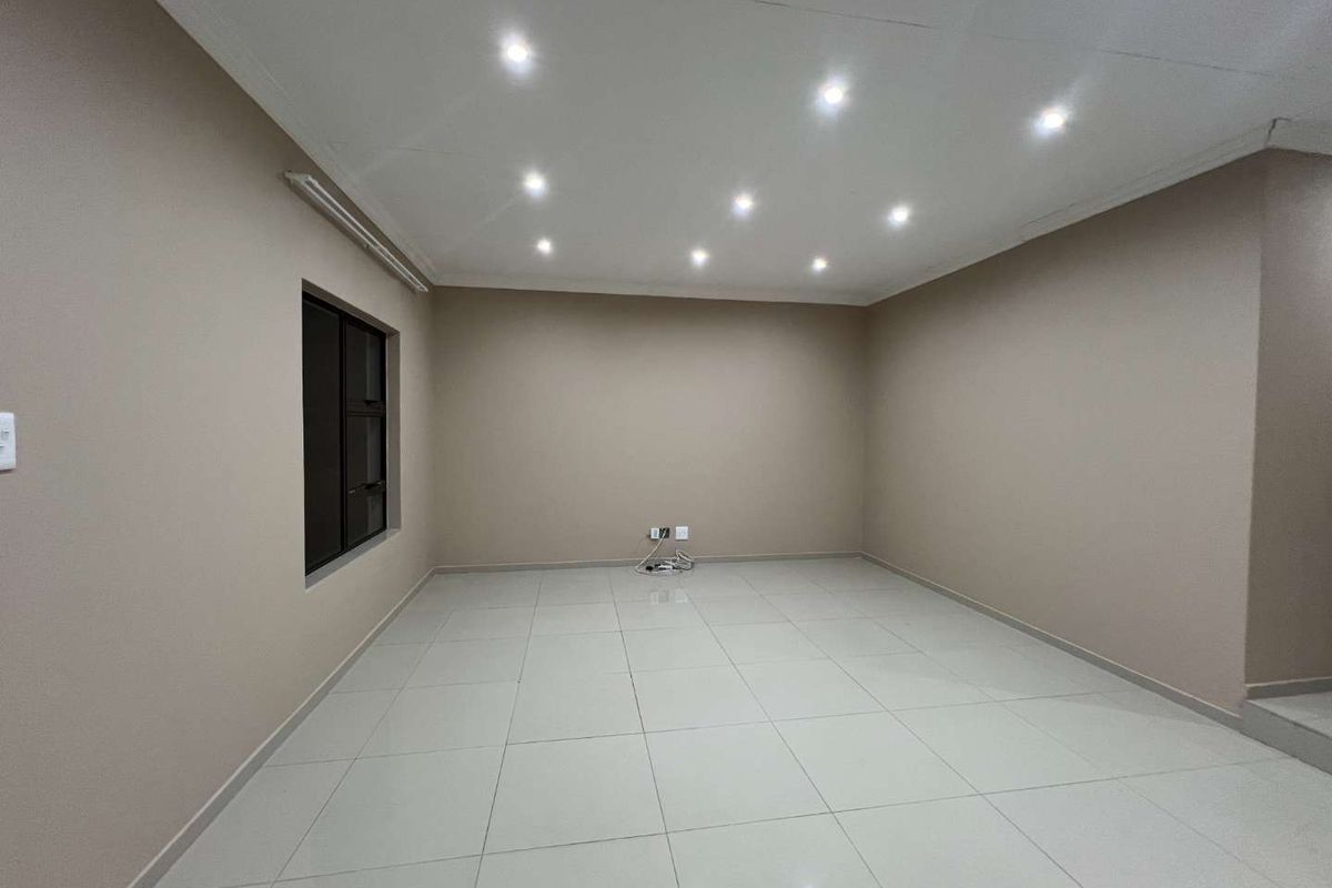 A spacious, empty living area featuring neutral wall tones, tiled flooring, and recessed ceiling downlights.