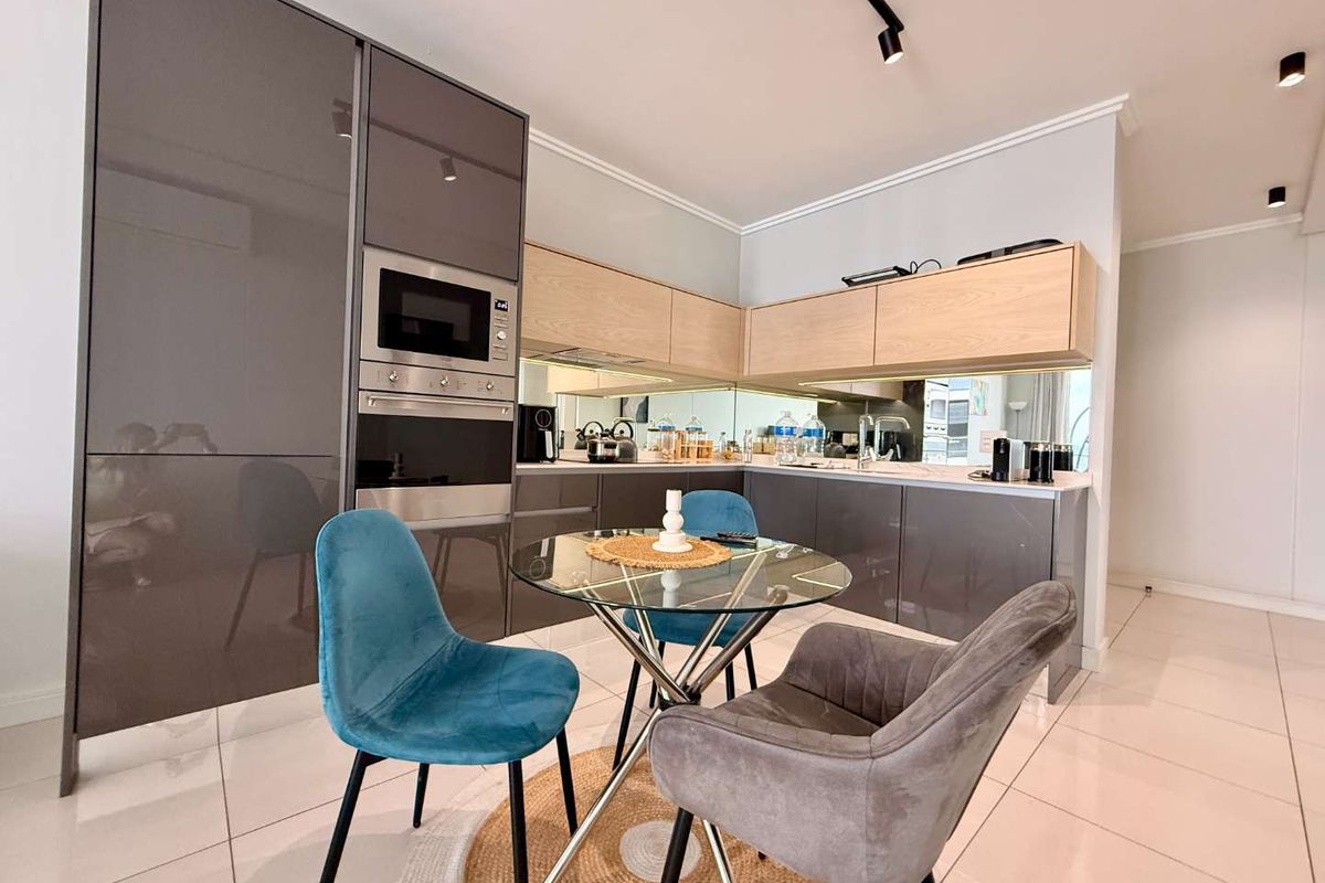 Modern kitchen featuring high-gloss cabinetry, integrated appliances, mirror splashback, and sleek track lighting, finished with polished floor tiles.