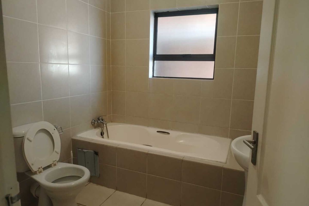 A functional bathroom featuring a bathtub, pedestal basin, and toilet with neutral wall and floor tiling.
