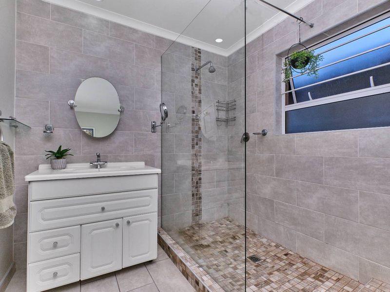 Modern bathroom featuring a white vanity cabinet, walk-in shower with glass screen, and neutral grey wall tiling with mosaic accents.