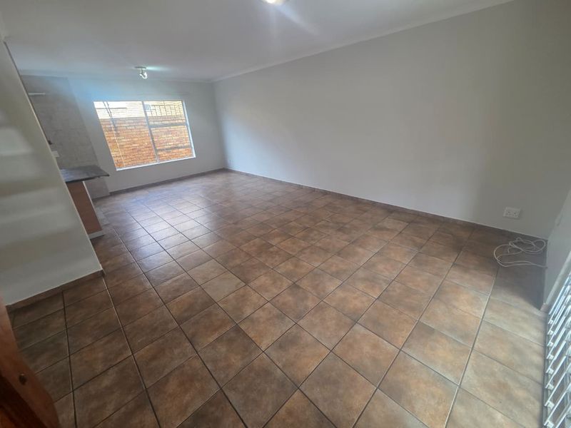 An open-plan living and kitchen area featuring neutral walls, tiled flooring, and a breakfast counter, offering a blank canvas for interior design.