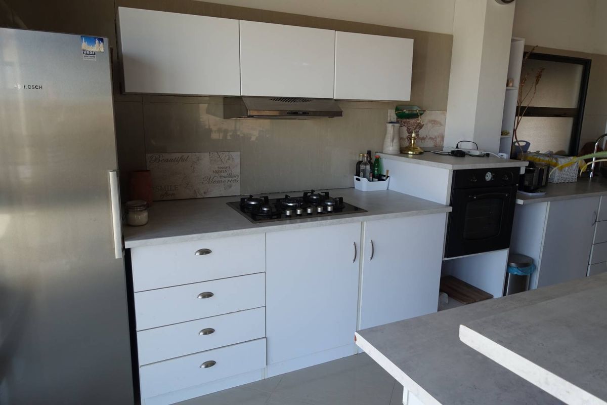 A functional kitchen featuring white cabinetry, a built-in gas hob, an extractor fan, and a wall-mounted oven with stone-look countertops.