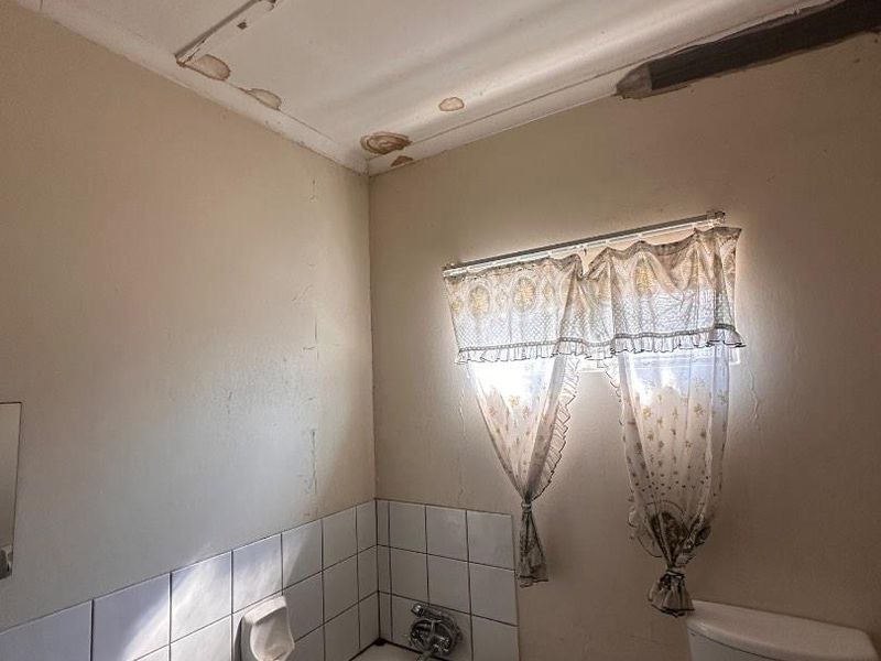 A dated bathroom featuring a standard bathtub and toilet, requiring significant renovation and repair to address ceiling water damage and wall surface deterioration.