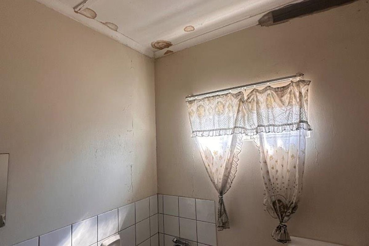 A dated bathroom featuring a standard bathtub and toilet, requiring significant renovation and repair to address ceiling water damage and wall surface deterioration.