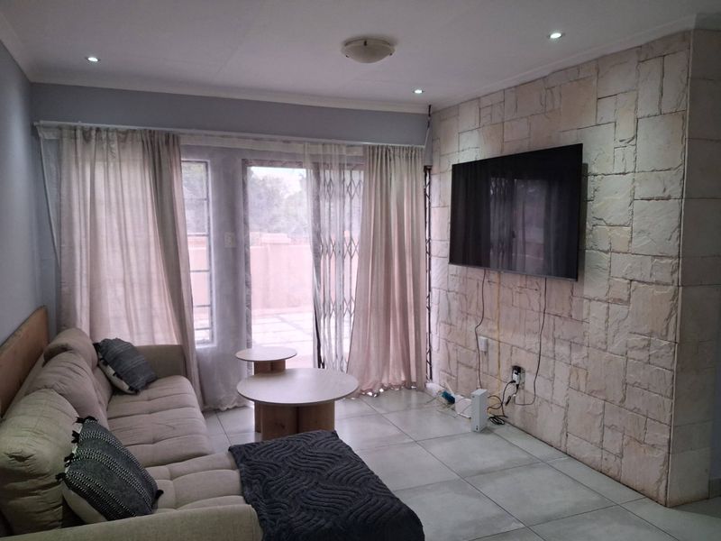 A living room featuring a textured stone accent wall, tiled flooring, and sliding glass doors providing access to the patio area.