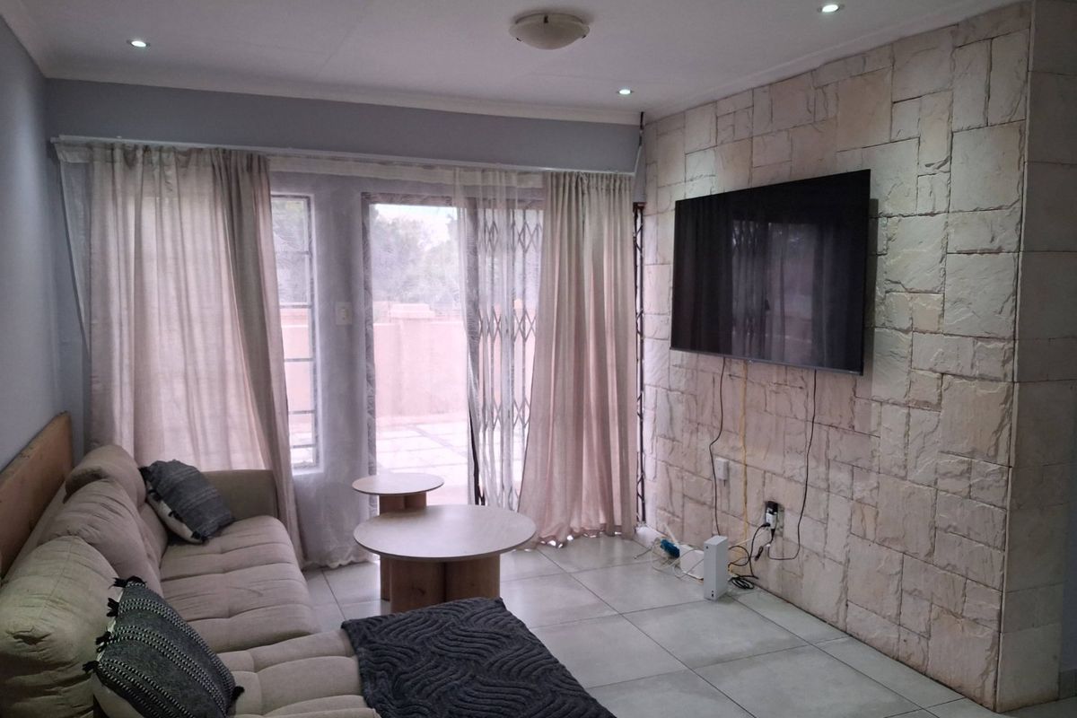 A living room featuring a textured stone accent wall, tiled flooring, and sliding glass doors providing access to the patio area.