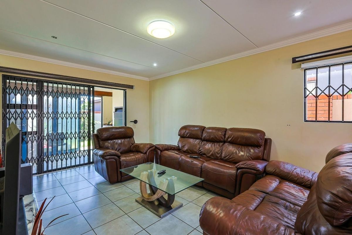 A living room featuring tiled flooring, a sliding glass door with security gate, and a window with security bars.