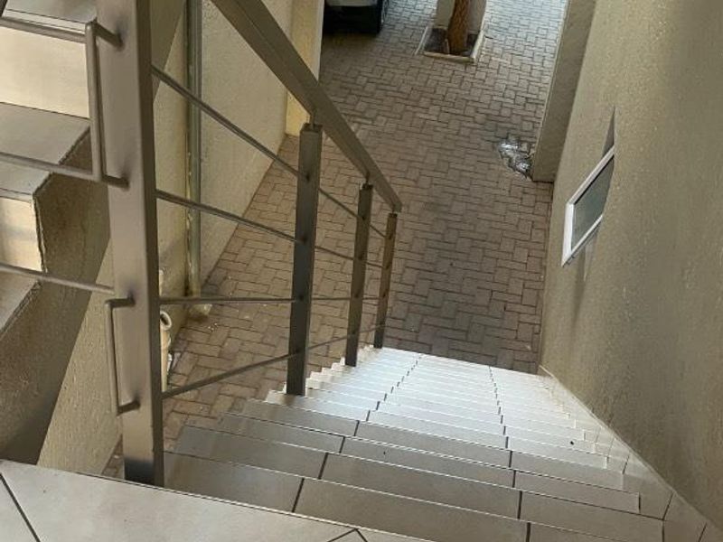 An exterior staircase with stainless steel balustrades leading down to a paved driveway area.