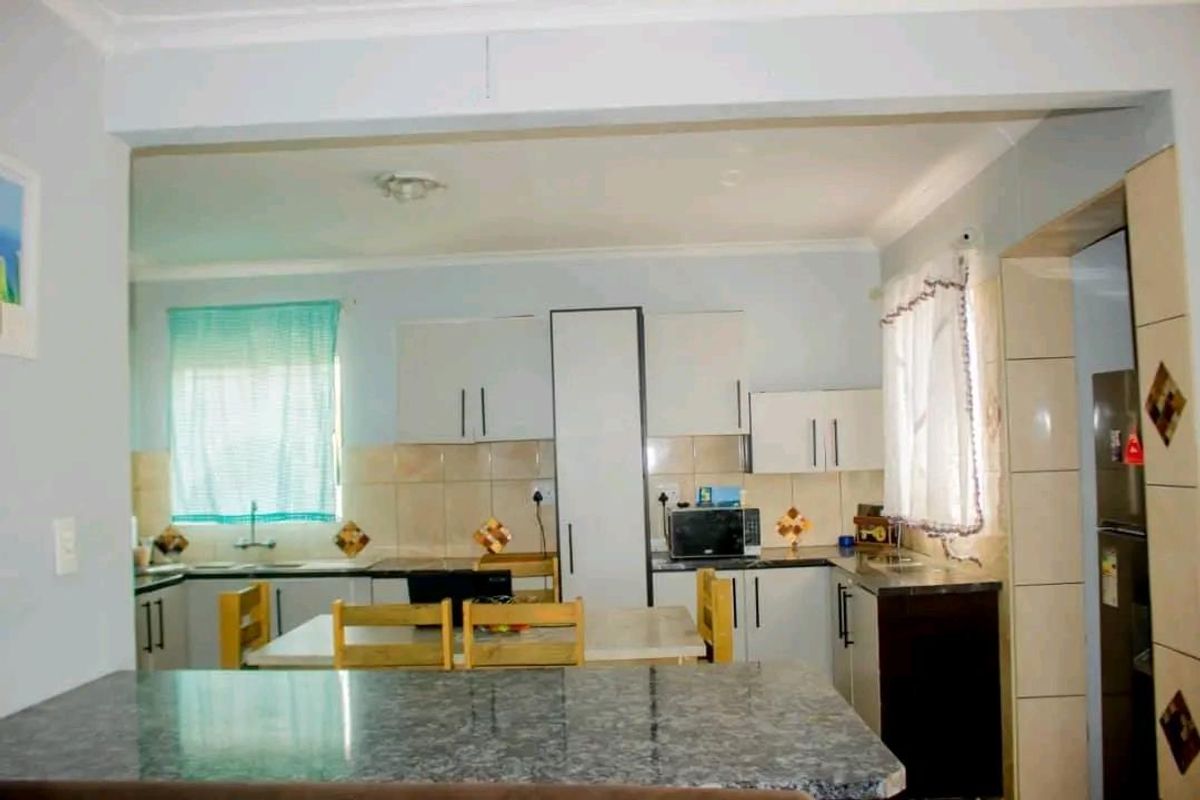 A functional kitchen featuring white cabinetry, tiled splashbacks, and a stone-look breakfast bar, offering a practical layout for daily meal preparation.