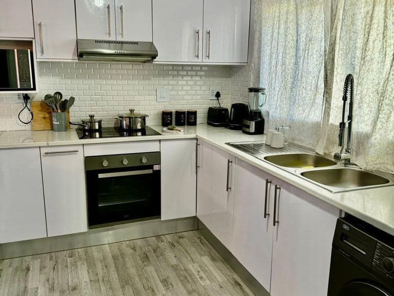Modern kitchen featuring white gloss cabinetry, subway tile backsplash, integrated appliances, and durable wood-look laminate flooring.