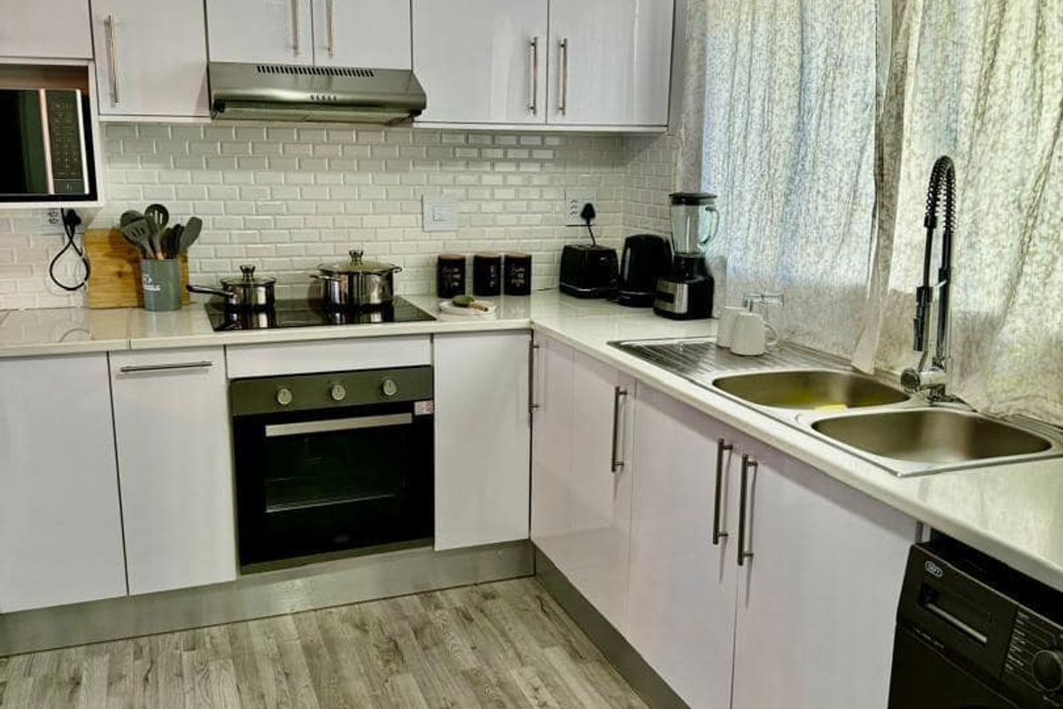 Modern kitchen featuring white gloss cabinetry, subway tile backsplash, integrated appliances, and durable wood-look laminate flooring.