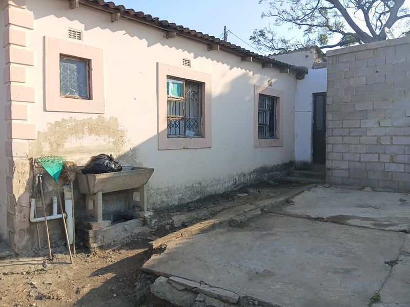 Rear exterior view of the property showing a concrete utility sink, weathered plaster walls, and a concrete patio area requiring maintenance.