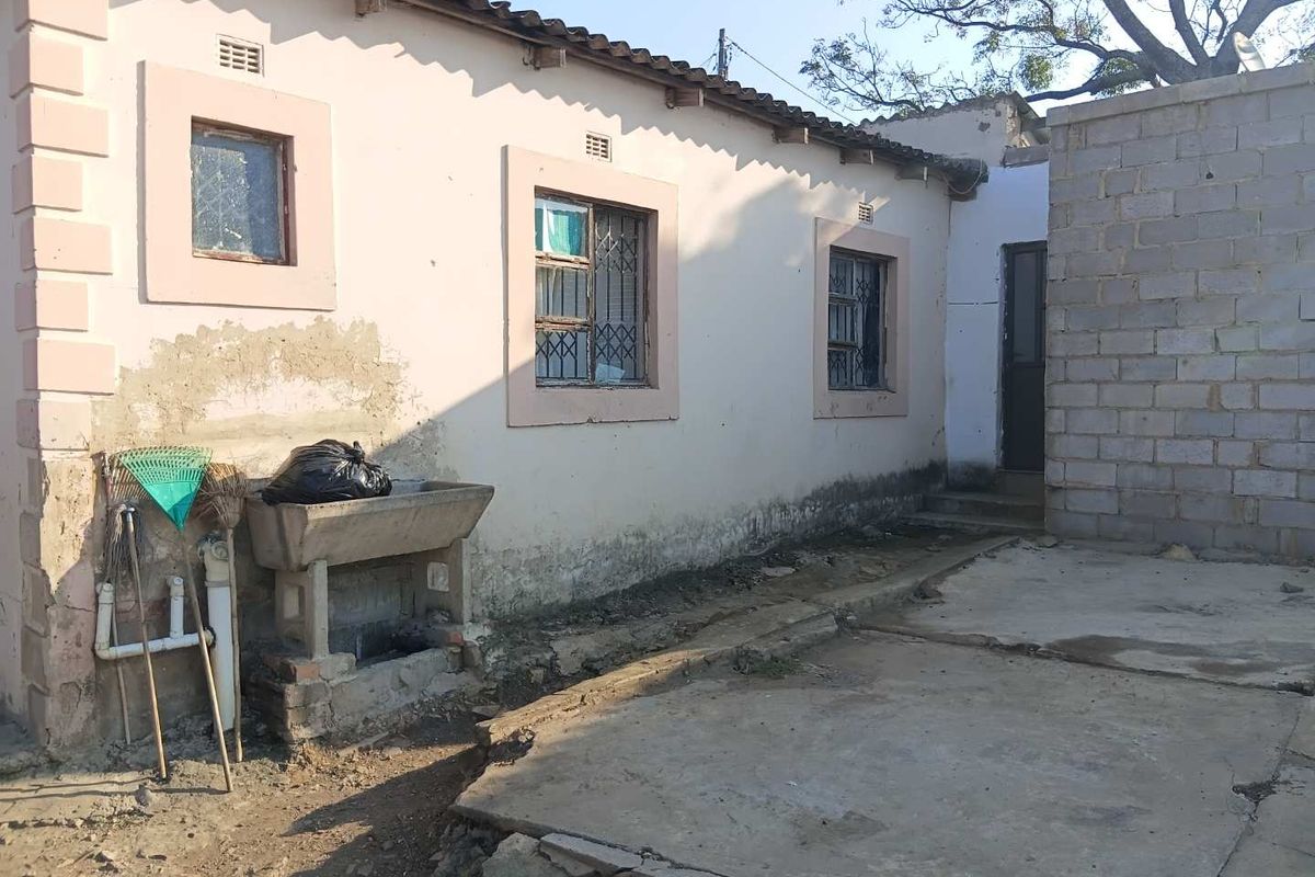 Rear exterior view of the property showing a concrete utility sink, weathered plaster walls, and a concrete patio area requiring maintenance.
