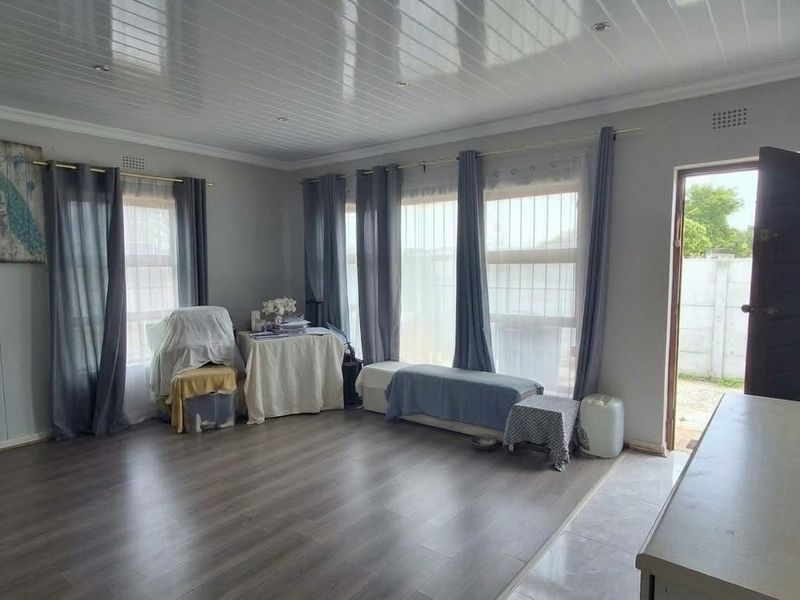 Spacious living area featuring durable laminate flooring, modern PVC ceiling panels with recessed lighting, and large windows with security bars.