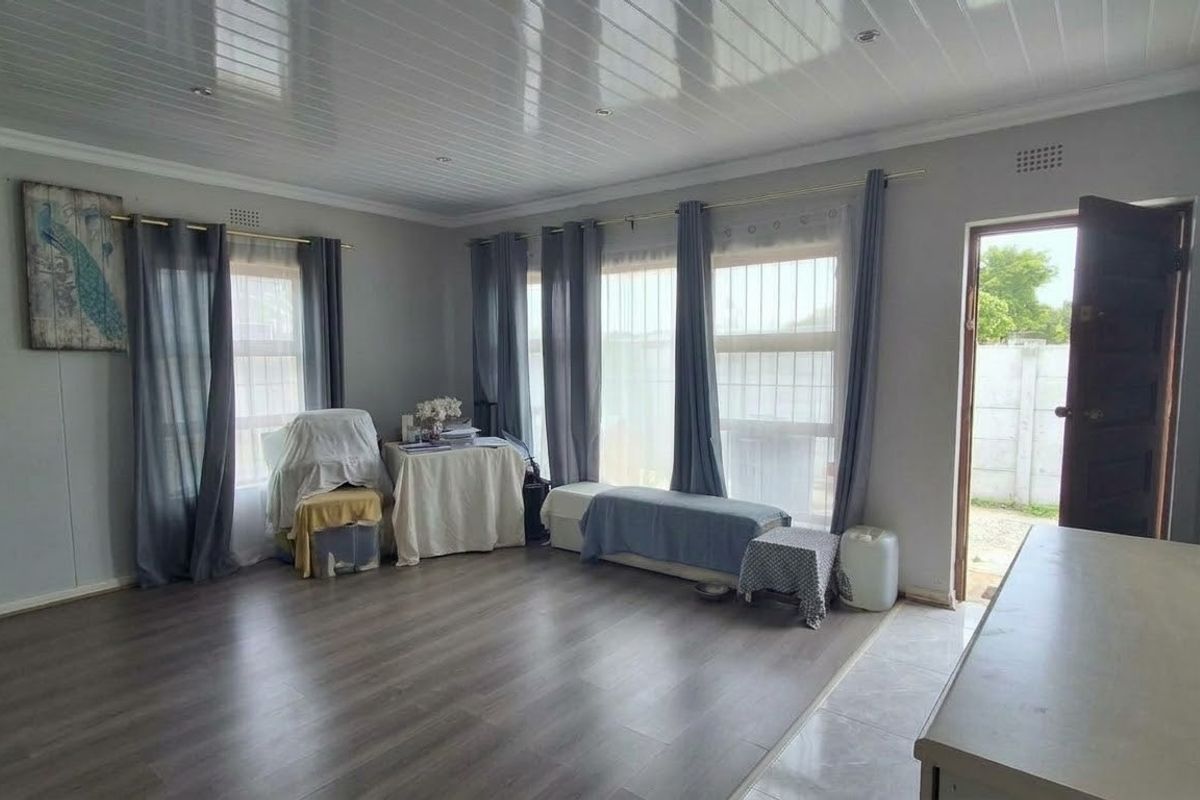 Spacious living area featuring durable laminate flooring, modern PVC ceiling panels with recessed lighting, and large windows with security bars.