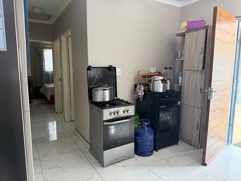A functional kitchen area featuring tiled flooring, a built-in pantry cupboard, and a freestanding gas stove with an electric oven.