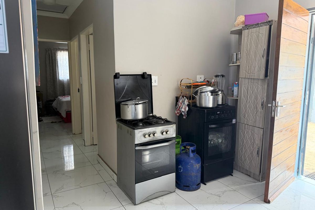 A functional kitchen area featuring tiled flooring, a built-in pantry cupboard, and a freestanding gas stove with an electric oven.